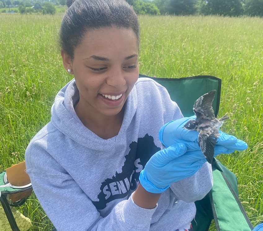 Rayah Stein sits outside and smiles while holding a baby bird.