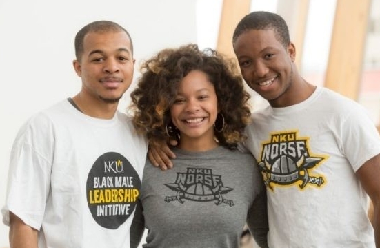 Three students stand together smiling, wearing NKU t-shirts.